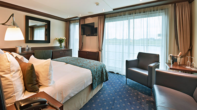 Dobbeltseng, sofagruppe og skrivebord p� Leonora. Utsikt gjennom store vinduer. 